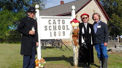 2019 Photo of three association members standing in front of the Cato School 1869 sign that is in front of the restored Cato Schoolhouse